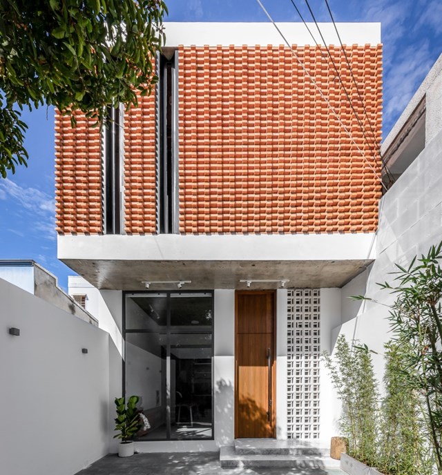 Phần mặt tiền được x&acirc;y bằng gạch nung gi&uacute;p l&agrave;m tăng vẻ đẹp cũng như tạo ấn tượng cho to&agrave;n bộ ng&ocirc;i nh&agrave;. Phần gạch được xếp đan, tạo luồng kh&ocirc;ng kh&iacute; đối lưu từ ngo&agrave;i v&agrave;o trong. B&ecirc;n cạnh đ&oacute;, bức tường hai b&ecirc;n được sơn trắng, l&agrave;m giảm sự hấp thụ &aacute;nh s&aacute;ng mặt trời.