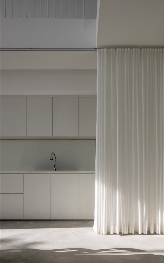 Tấm r&egrave;m trắng k&eacute;o d&agrave;i từ trần đến s&agrave;n được bố tr&iacute; để che đi khu bếp khi gia chủ cần sử dụng kh&ocirc;ng gian để trưng b&agrave;y