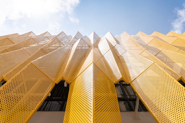 Để giải quyết ảnh hưởng nhiệt độ cao g&acirc;y ra bởi &aacute;nh nắng mặt trời chiếu thẳng v&agrave;o t&ograve;a nh&agrave;, giới kiến tr&uacute;c sư đ&atilde; thiết kế cấu tr&uacute;c k&eacute;p gồm c&aacute;c bức tường k&iacute;nh v&agrave; tấm nh&ocirc;m đục lỗ bằng đồ họa.