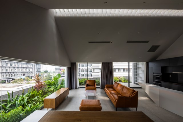 Ph&ograve;ng kh&aacute;ch v&agrave; bếp được kiến tr&uacute;c sư thiết kế mở tạo kh&ocirc;ng gian th&ocirc;ng tho&aacute;ng. Khu vực tiếp kh&aacute;ch b&agrave;y tr&iacute; nội thất gỗ giản đơn, c&ugrave;ng ghế sofa bọc da n&acirc;u.