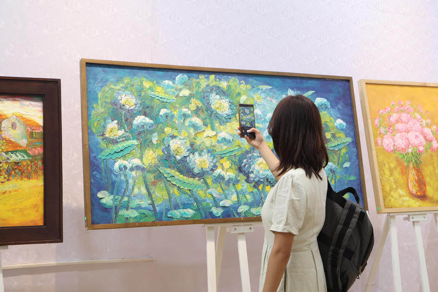 Một khách tham quan dùng điện thoại ghi lại hình ảnh tác phẩm hội họa lấy cảm hứng từ hoa sen tại triển lãm.